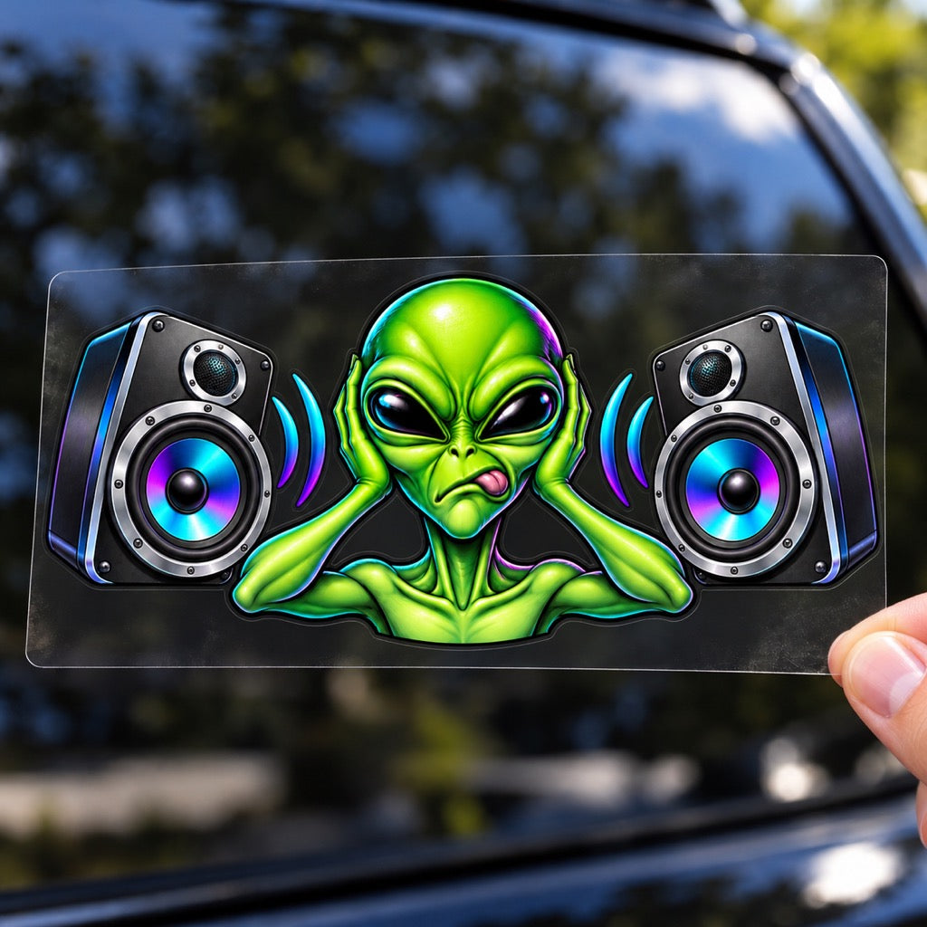 Ръка държи стикер Alien Bass с извънземно и две тонколони върху плоско прозрачно транспортно фолио